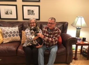 A man and woman sitting on top of a couch holding a dog.