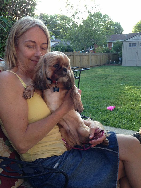 A woman holding her dog in the backyard.