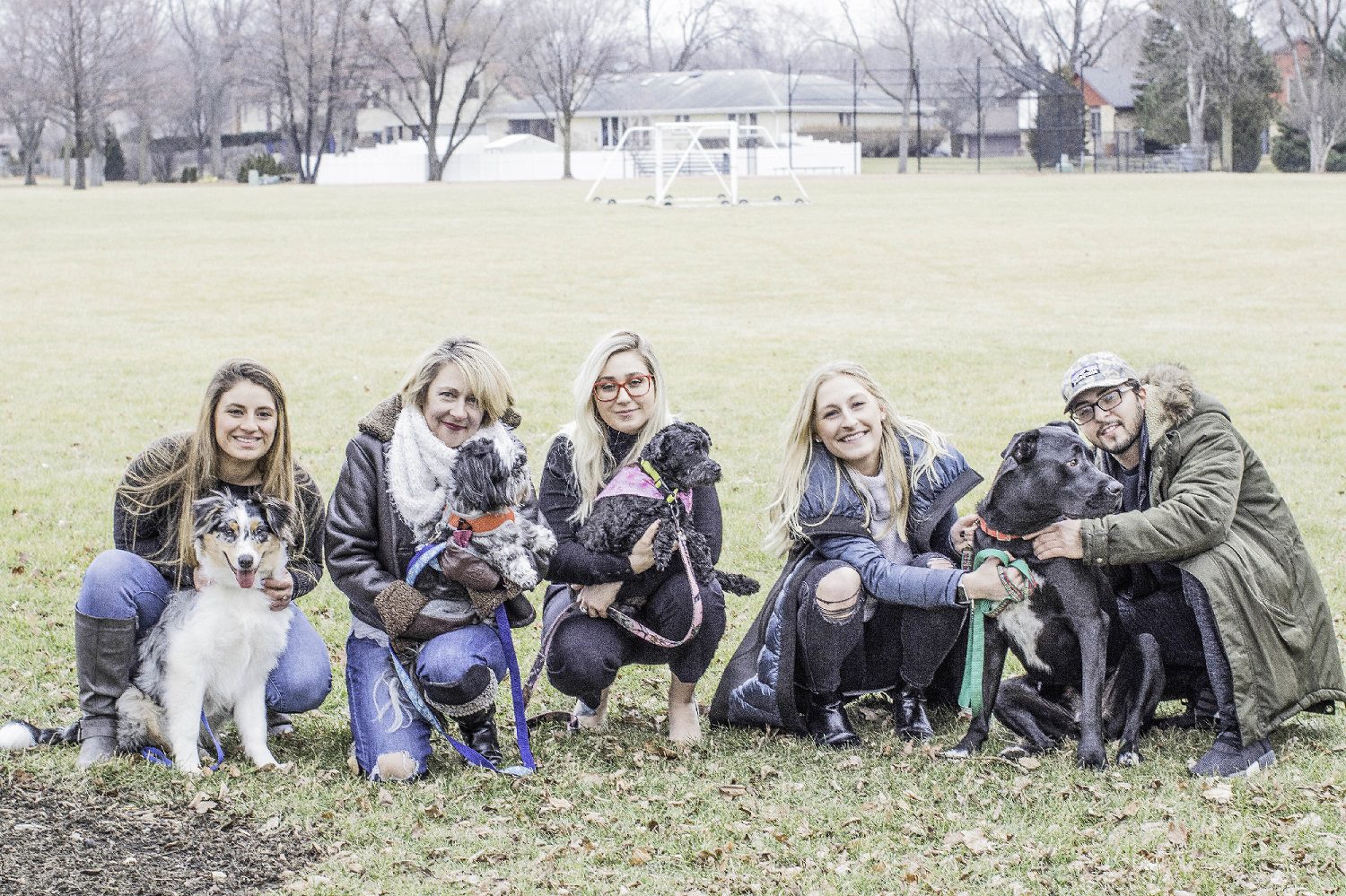 A group of people kneeling down with dogs.