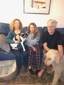 A family sitting on the couch with their dog.